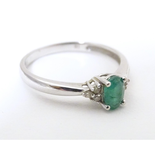 592 - A 10ct white gold ring set with central emerald flanked by three diamonds each shoulder. Ring size a... 