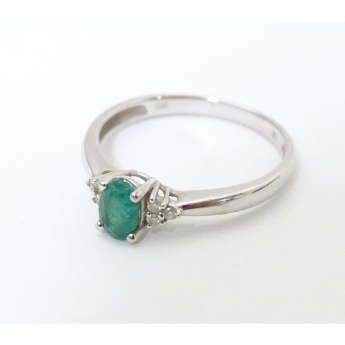 592 - A 10ct white gold ring set with central emerald flanked by three diamonds each shoulder. Ring size a... 