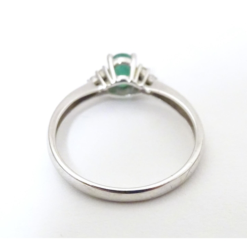 592 - A 10ct white gold ring set with central emerald flanked by three diamonds each shoulder. Ring size a... 