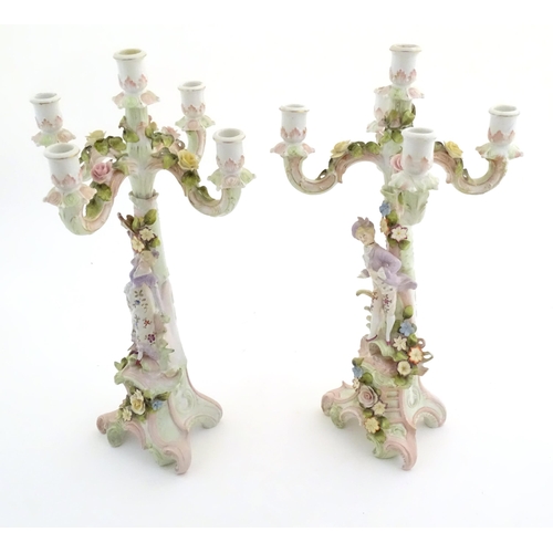 159 - A pair of Continental porcelain candelabra / candelabrum with figural and floral decoration, one wit... 