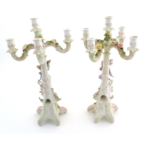 159 - A pair of Continental porcelain candelabra / candelabrum with figural and floral decoration, one wit... 