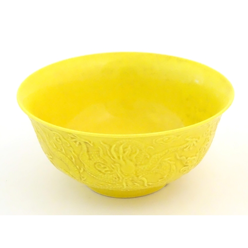 9 - A Chinese bowl with a yellow ground decorated in relief with dragons amongst stylised clouds. Charac... 