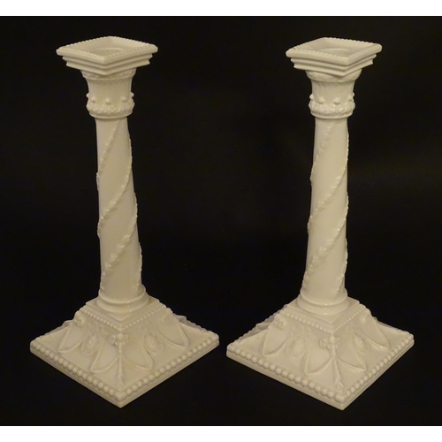 94 - A pair of Royal Worcester candlesticks with relief twist decoration to columns and swag detail to sq... 