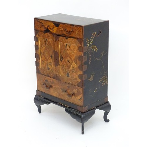 298 - An oriental black lacquered cabinet with carrying handles to the side and resting on a stand. The do... 