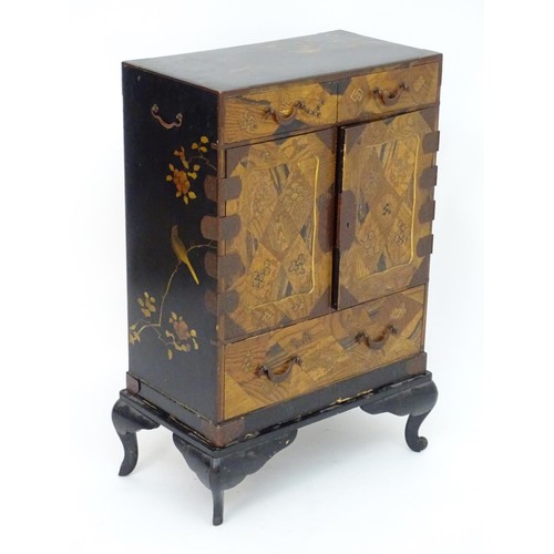 298 - An oriental black lacquered cabinet with carrying handles to the side and resting on a stand. The do... 