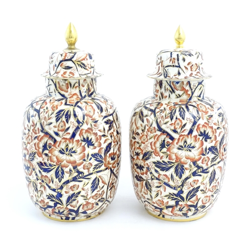 128 - A pair of Royal Crown Derby style lidded vases / urns decorated in the Imari palette with flowers an... 