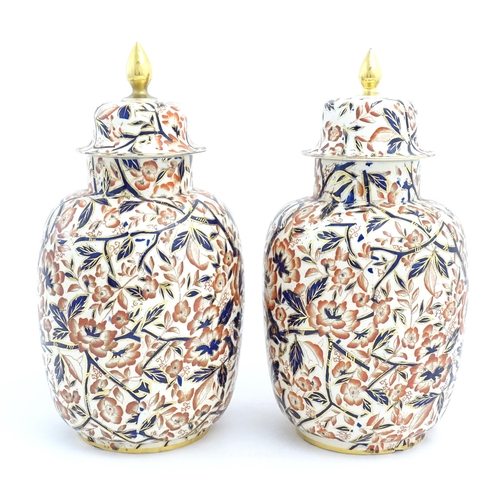 128 - A pair of Royal Crown Derby style lidded vases / urns decorated in the Imari palette with flowers an... 