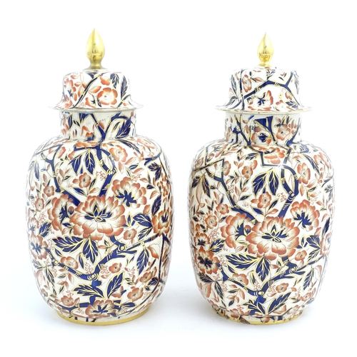 128 - A pair of Royal Crown Derby style lidded vases / urns decorated in the Imari palette with flowers an... 