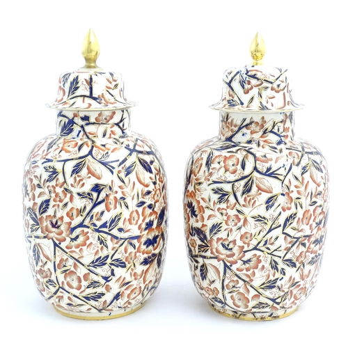 128 - A pair of Royal Crown Derby style lidded vases / urns decorated in the Imari palette with flowers an... 