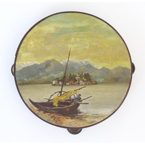 897 - A 20thC tambourine, the drum painted in oils depicting a Continental lake scene with fisherman, boat... 