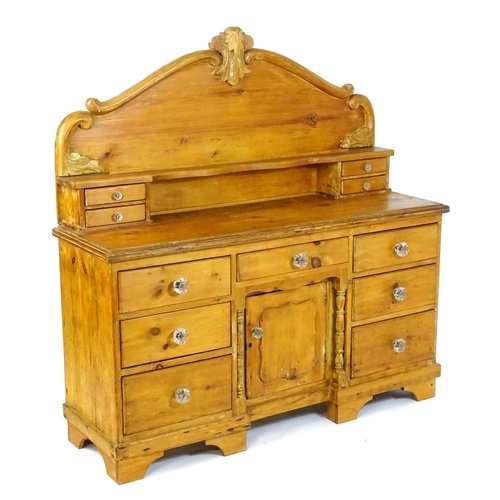 A Victorian pine dresser with a shaped carved upstand above two opposing sets of small drawers, the base made up of two banks of three short graduated drawers with an additional small drawer and cupboards to the base, all adorned with glass knob handles. 58" wide x 19" deep x 58" high.
