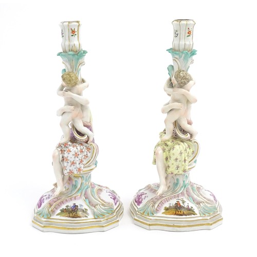 96A - A pair of Continental porcelain figural candlesticks on shaped bases with scrolling floral and folia... 