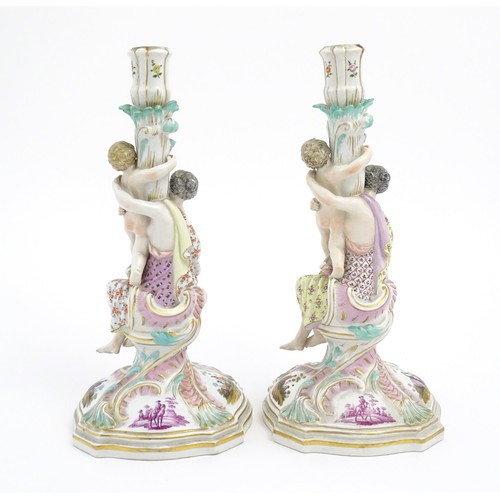 96A - A pair of Continental porcelain figural candlesticks on shaped bases with scrolling floral and folia... 