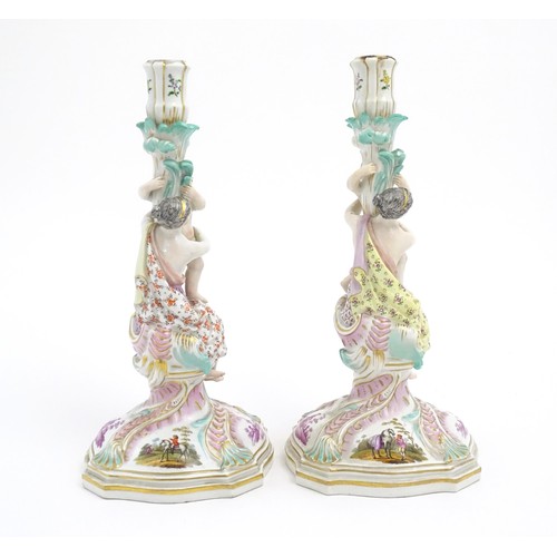 96A - A pair of Continental porcelain figural candlesticks on shaped bases with scrolling floral and folia... 