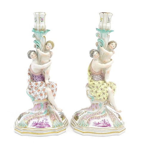 96A - A pair of Continental porcelain figural candlesticks on shaped bases with scrolling floral and folia... 