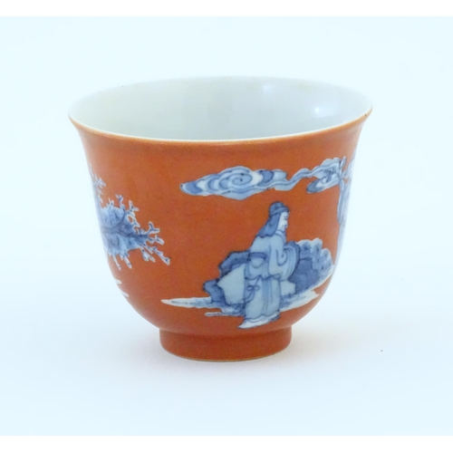 22 - A Chinese tea bowl with a red ground decorated in blue with figures in a landscape. Character marks ... 