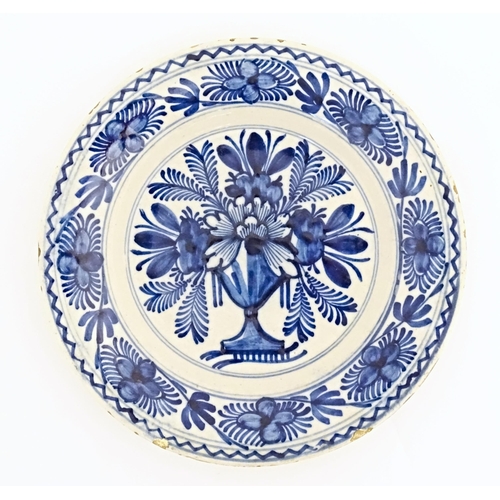 57 - A Delft blue and white plate decorated with central bouquet of flowers in a vase, bordered by stylis... 