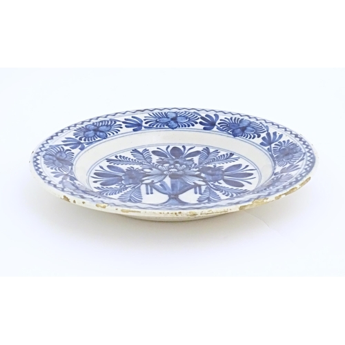 57 - A Delft blue and white plate decorated with central bouquet of flowers in a vase, bordered by stylis... 