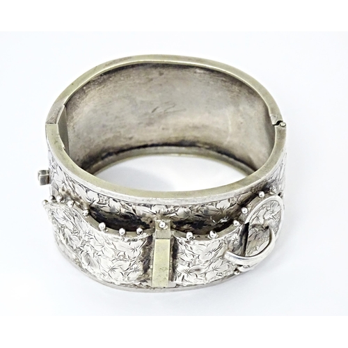 630 - A white metal bangle bracelet with buckle detail and engraved foliate decoration.