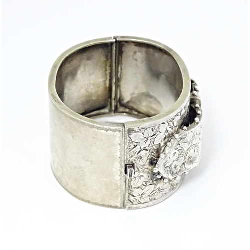 630 - A white metal bangle bracelet with buckle detail and engraved foliate decoration.