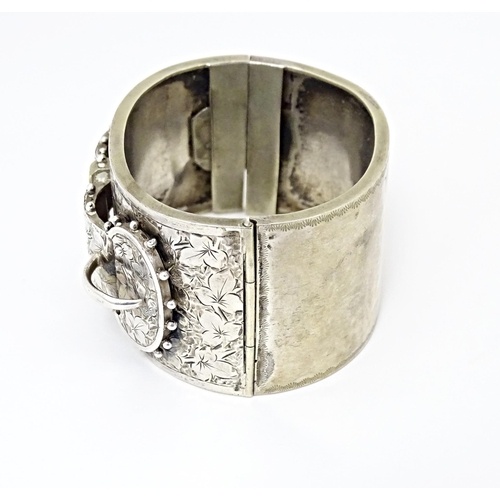 630 - A white metal bangle bracelet with buckle detail and engraved foliate decoration.