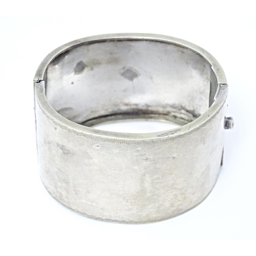 630 - A white metal bangle bracelet with buckle detail and engraved foliate decoration.