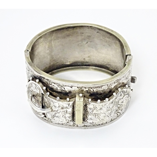 630 - A white metal bangle bracelet with buckle detail and engraved foliate decoration.