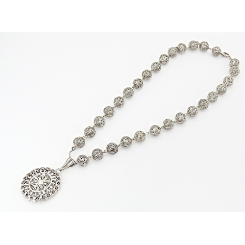 632 - A silver and white metal filigreed bead necklace, with oval filigree pendant locket. Approx. 20