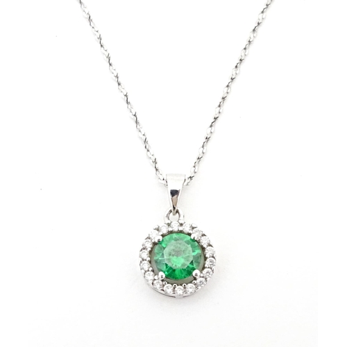 702 - A silver suite of jewellery comprising pendant and stud earrings set with central green stone border... 