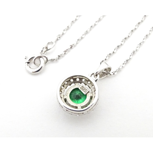 702 - A silver suite of jewellery comprising pendant and stud earrings set with central green stone border... 