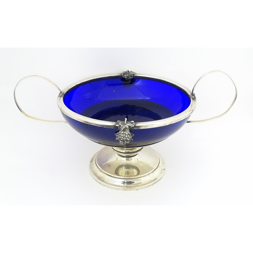 534 - A silver plate pedestal bowl with twin handles and fruiting vine decoration, with blue glass liner. ... 