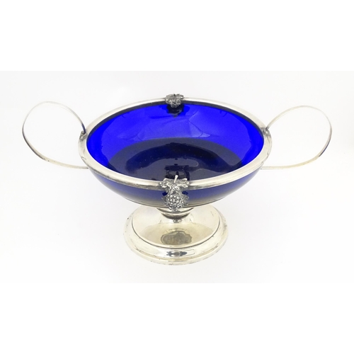 534 - A silver plate pedestal bowl with twin handles and fruiting vine decoration, with blue glass liner. ... 