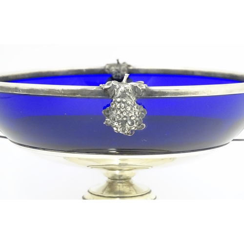 534 - A silver plate pedestal bowl with twin handles and fruiting vine decoration, with blue glass liner. ... 