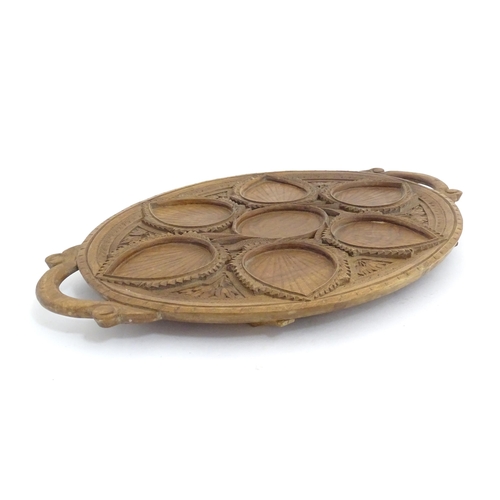 1025 - A carved wooden tray of oval form with scrolled handles, carved foliate decoration and seven section... 