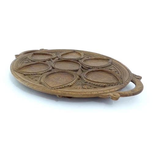 1025 - A carved wooden tray of oval form with scrolled handles, carved foliate decoration and seven section... 