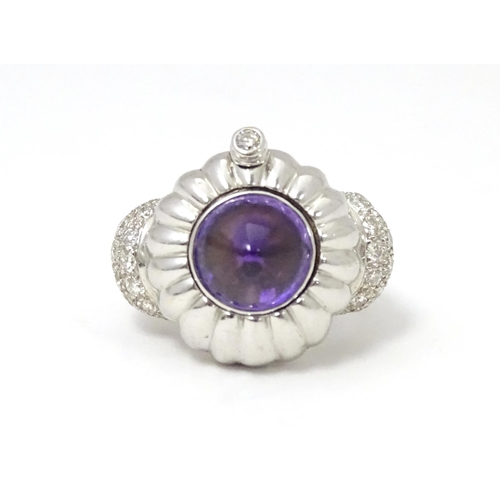 551 - An unusual 18ct white gold ring set with amethyst cabochon flanked by diamonds to shoulders. The top... 