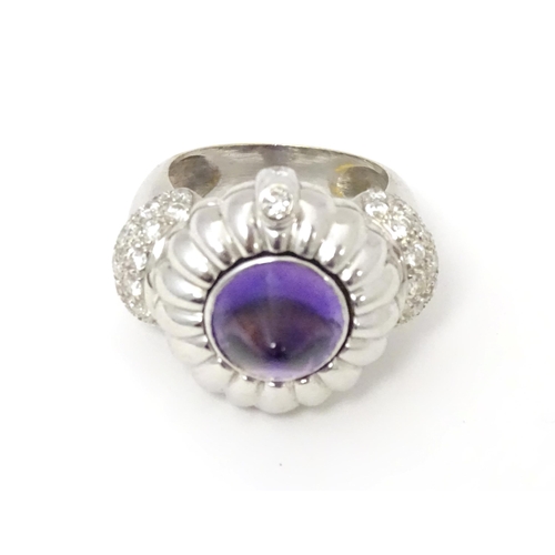 551 - An unusual 18ct white gold ring set with amethyst cabochon flanked by diamonds to shoulders. The top... 