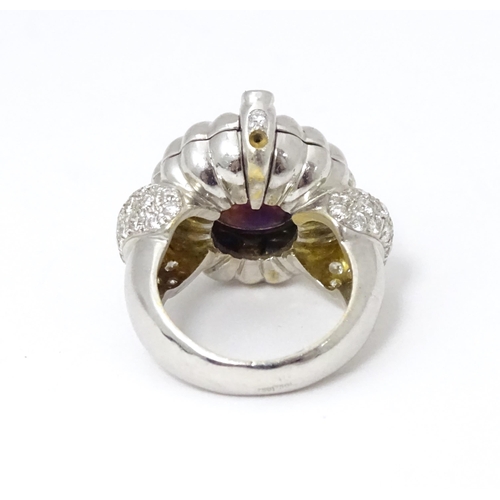 551 - An unusual 18ct white gold ring set with amethyst cabochon flanked by diamonds to shoulders. The top... 