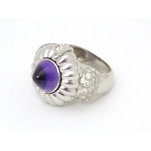 551 - An unusual 18ct white gold ring set with amethyst cabochon flanked by diamonds to shoulders. The top... 