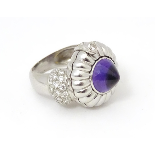 551 - An unusual 18ct white gold ring set with amethyst cabochon flanked by diamonds to shoulders. The top... 