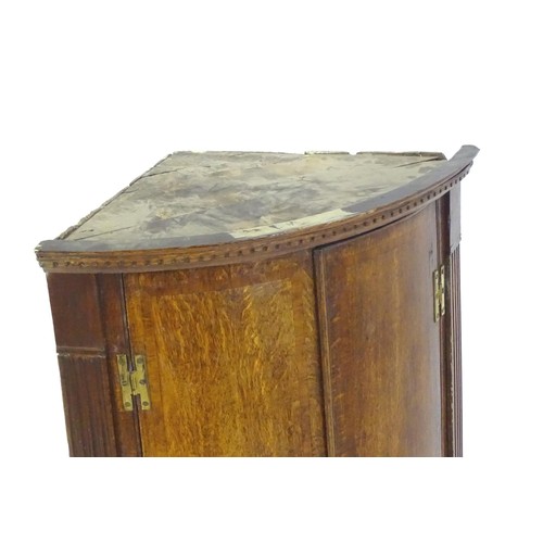 142 - A George III oak bow fronted corner cupboard with crossbanded decoration and H - bracket hinges. 27