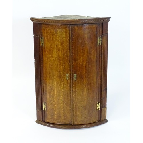 142 - A George III oak bow fronted corner cupboard with crossbanded decoration and H - bracket hinges. 27