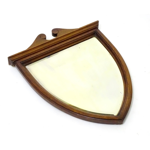19 - An early 20thC oak wall mirror of shield shape with a bevelled glass centre. 15