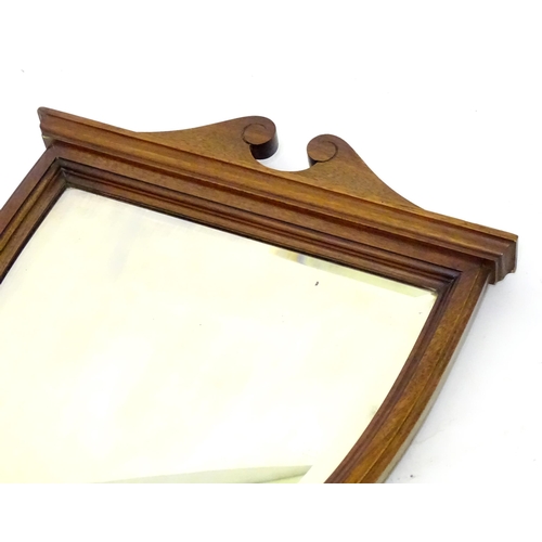 19 - An early 20thC oak wall mirror of shield shape with a bevelled glass centre. 15