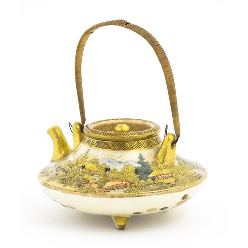 15 - A small Japanese Satsuma sake or tea pot of squat form raised on three feet, decorated with figures ... 