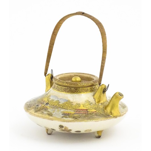 15 - A small Japanese Satsuma sake or tea pot of squat form raised on three feet, decorated with figures ... 