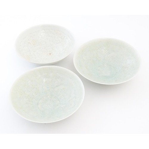 28 - Three Chinese celadon bowls of conical form with incised decoration depicting stylised children and ... 