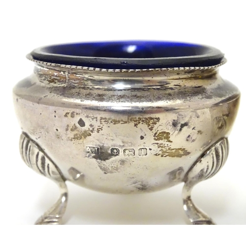 556 - A pair of circular silver table salts, each raised on three hoof feet, with blue glass liners and ma... 