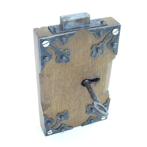 1253 - An 18thC door lock mechanism and key, with fittings, mounted to an oak panel with trefoil decoration... 