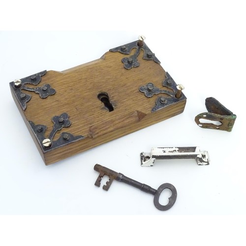 1253 - An 18thC door lock mechanism and key, with fittings, mounted to an oak panel with trefoil decoration... 